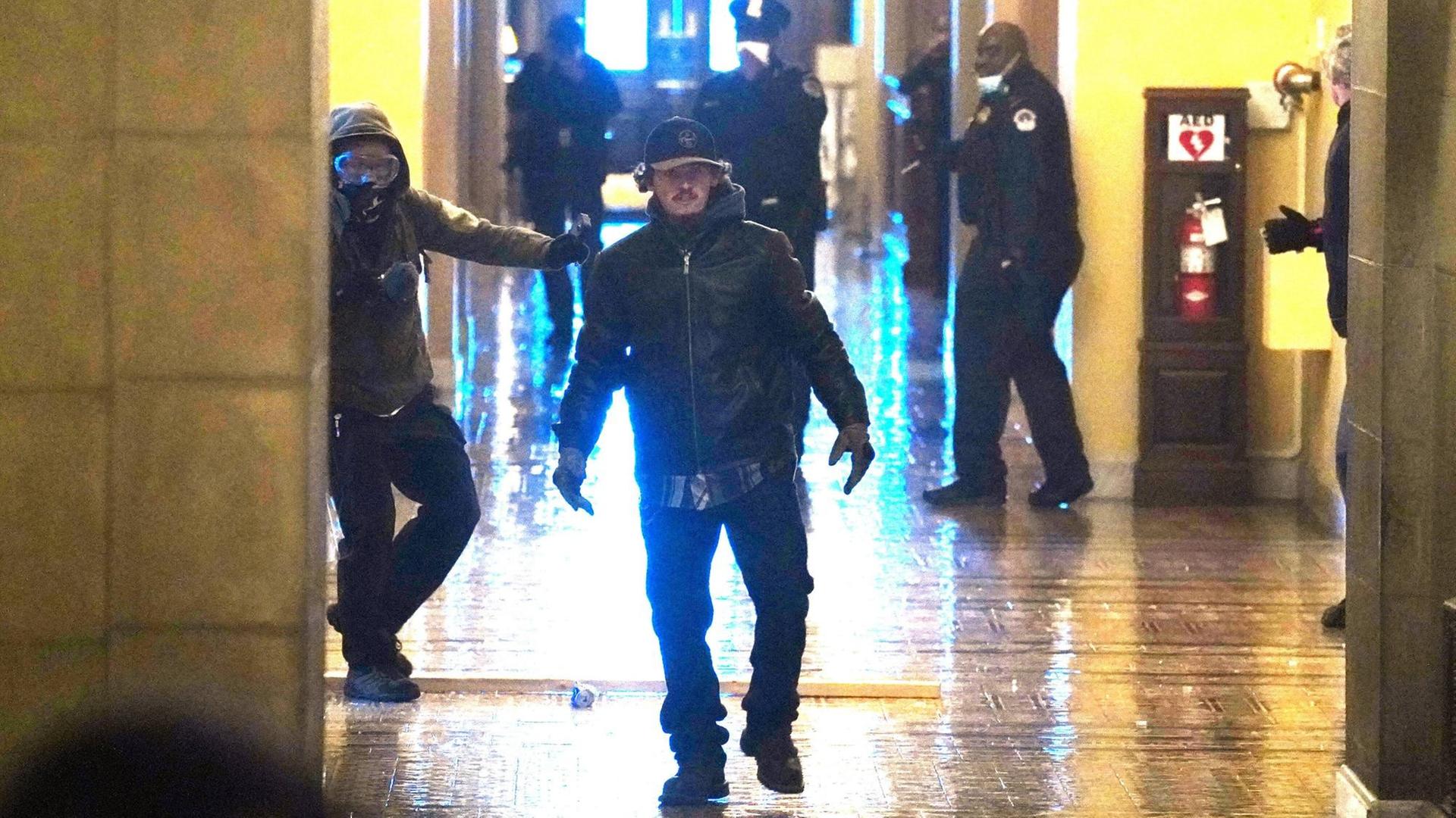 Zwei Protestler, die ins Kapitol eingedrungen sind, laufen auf die Kamera zu. Im Hintergrund stehen Polizisten. Zwei Protestler, die ins Kapitol eingedrungen sind, laufen auf die Kamera zu. Im Hintergrund stehen Polizisten.
