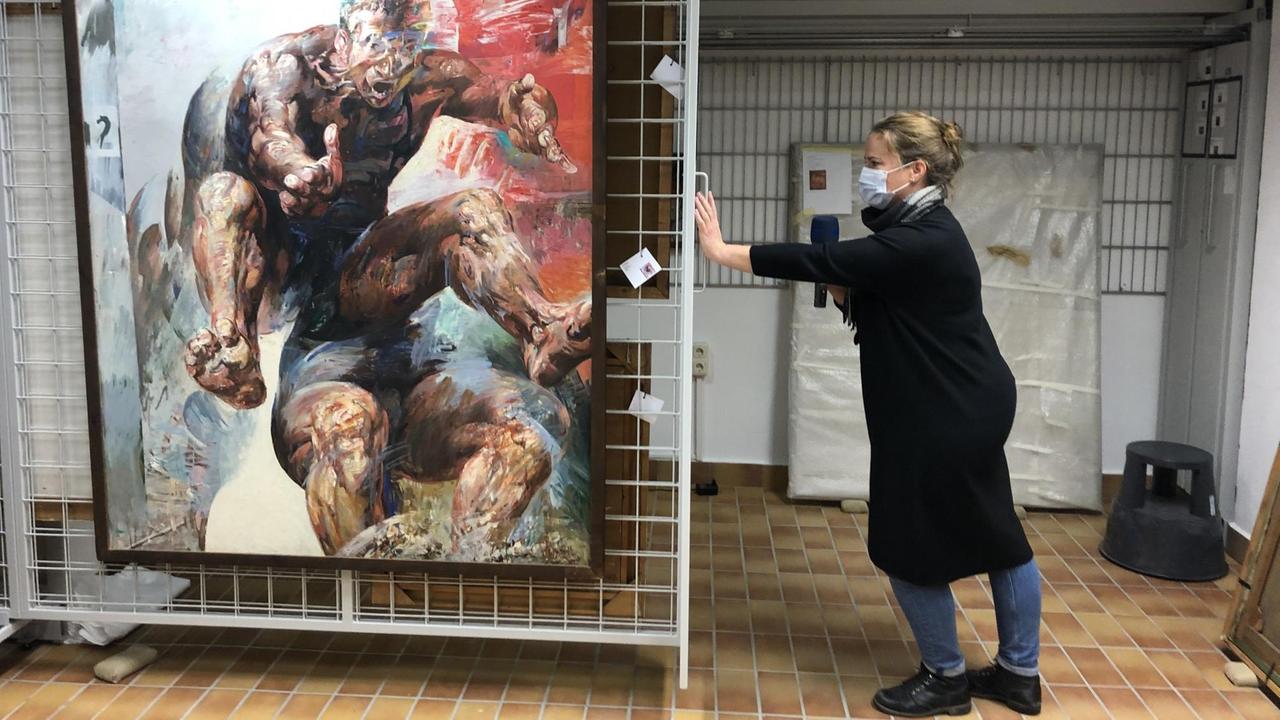 Eine Frau präsentiert ein großes Gemälde im Keller der Universität