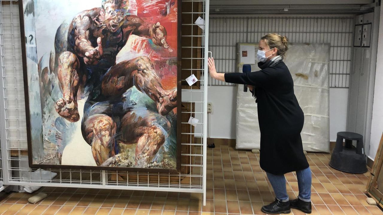 Eine Frau präsentiert ein großes Gemälde im Keller der Universität Eine Frau präsentiert ein großes Gemälde im Keller der Universität