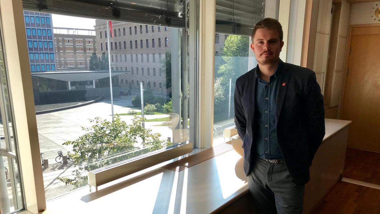 Ein junger schlanker Mann in dunklem Jacket steht am geöffneten Fenster, durch das die Sonne scheint. Im Hintergrund sieht man den Hof des Ministeriums. Ein junger schlanker Mann in dunklem Jacket steht am geöffneten Fenster, durch das die Sonne scheint. Im Hintergrund sieht man den Hof des Ministeriums.