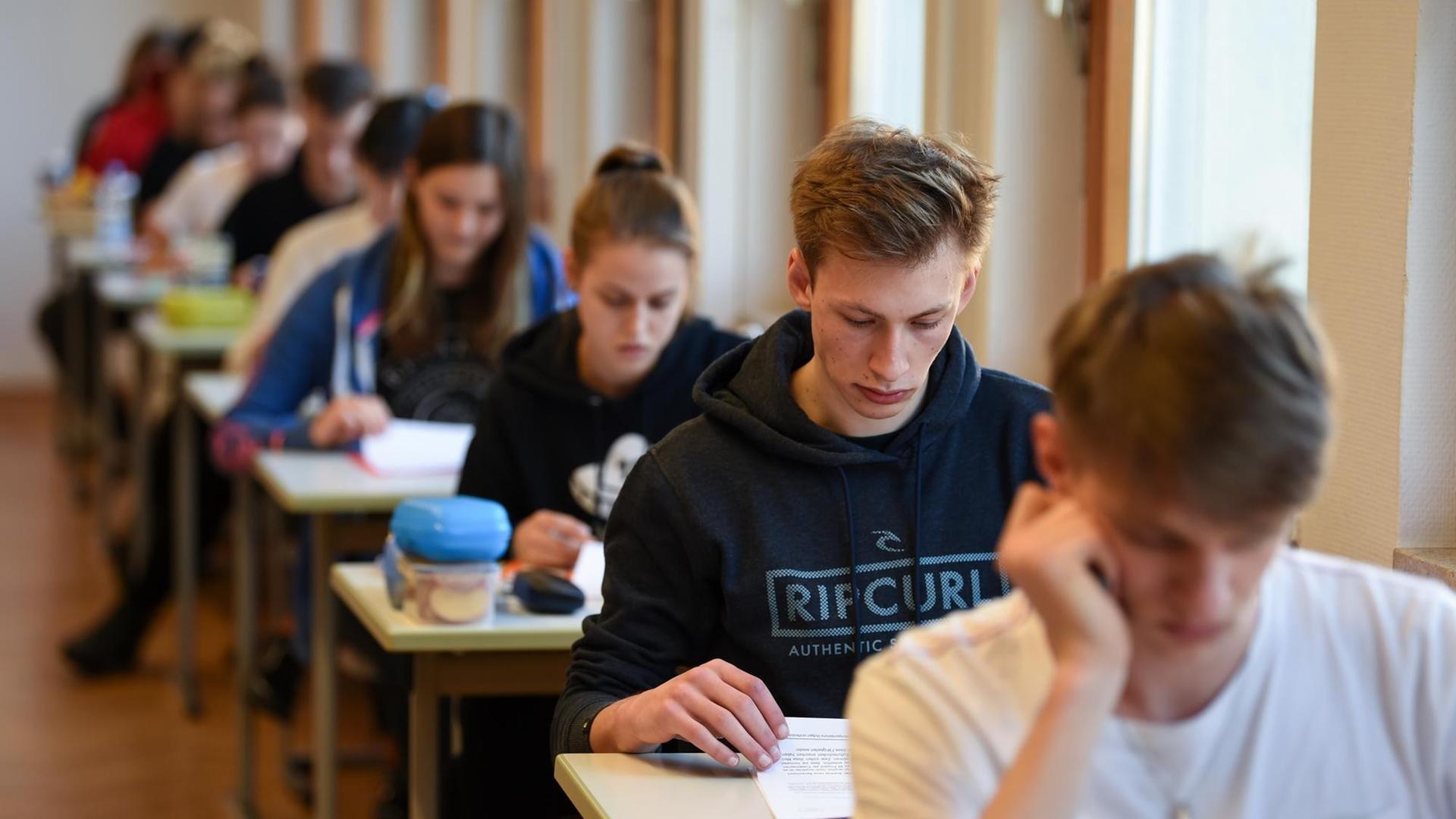 Abiturienten sitzen an Einzeltischen hintereinander und schauen die Prüfungensaufgaben im Fach Deutsch an.