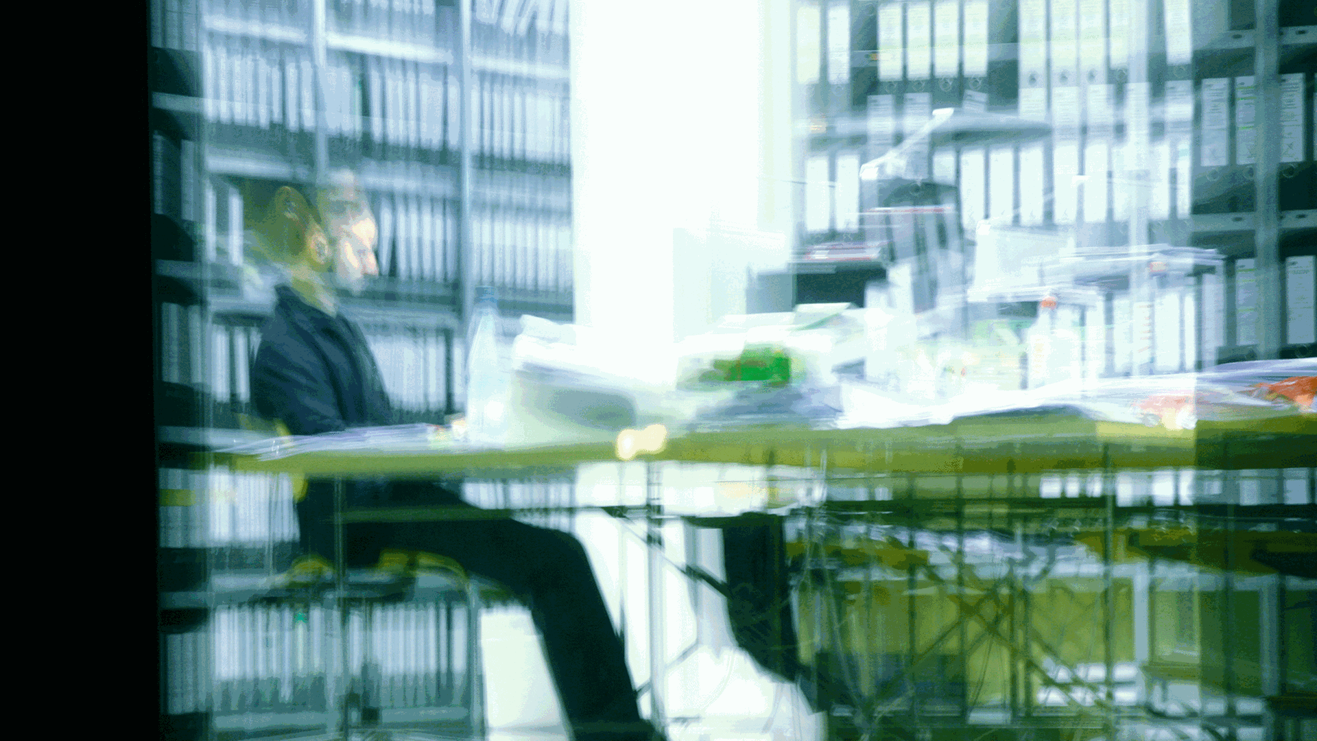 Ein Mann sitzt abends in einem Büro an einem vollen Schreibtisch und arbeitet.