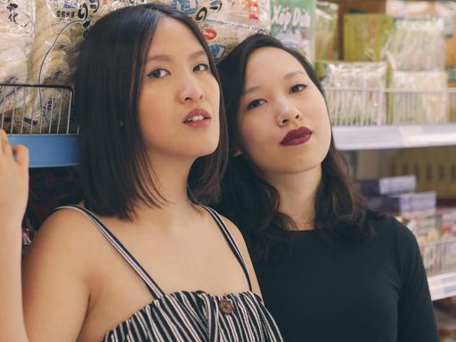 Vanessa Vu (rechts) und Minh Thu Tran (links) lehnen an einem Supermarkt-Regal mit asiatischen Lebensmitteln.