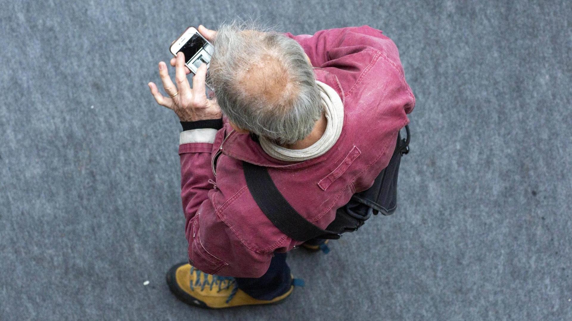 Ein Mann schaut mit gesenktem Kopf auf sein Smartphone Ein Mann schaut mit gesenktem Kopf auf sein Smartphone