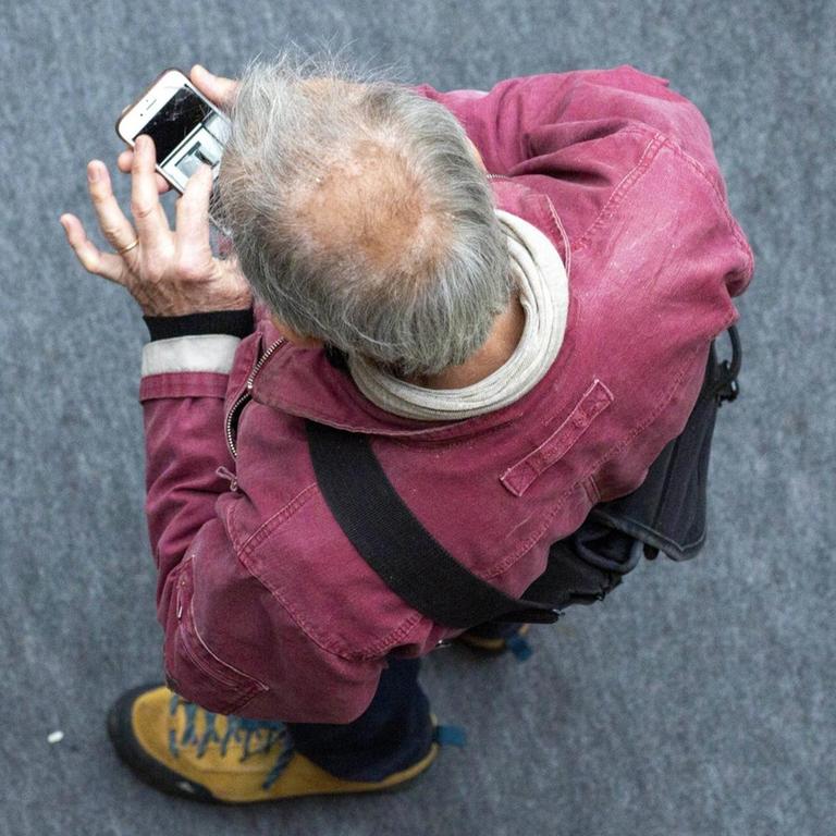 Ein Mann schaut mit gesenktem Kopf auf sein Smartphone