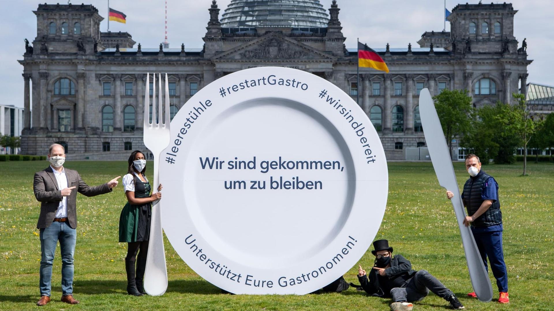 Vertreter des Gastronomie-Gewerbes stehen neben einem großen Teller mit der Aufschrift "Wir sind gekommen, um zu bleiben. Unterstützt Eure Gastronomen!" vor dem Deutschen Bundestag. Vertreter des Gastronomie-Gewerbes stehen neben einem großen Teller mit der Aufschrift "Wir sind gekommen, um zu bleiben. Unterstützt Eure Gastronomen!" vor dem Deutschen Bundestag.