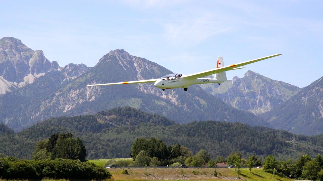Ein Segelflugzeug schwebt durch die Luft vor einem Bergpanorama. Ein Segelflugzeug schwebt durch die Luft vor einem Bergpanorama.