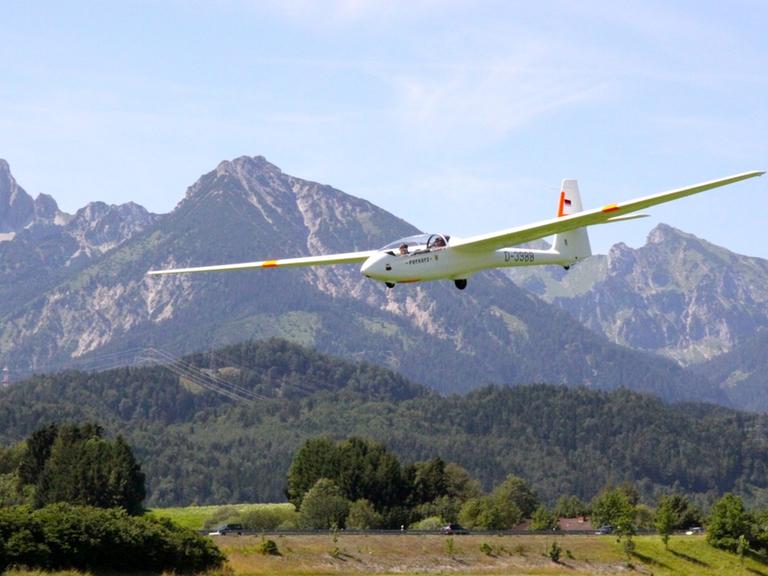Ein Segelflugzeug schwebt durch die Luft vor einem Bergpanorama.