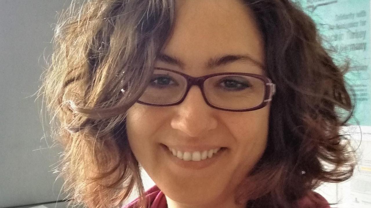 Olga Hünler lacht in die Kamera. Sie trägt einen rosa Schal. Im Hintergrund hängt ein Poster zu poltischem Engagemet und Wissenschaft. Olga Hünler lacht in die Kamera. Sie trägt einen rosa Schal. Im Hintergrund hängt ein Poster zu poltischem Engagemet und Wissenschaft.
