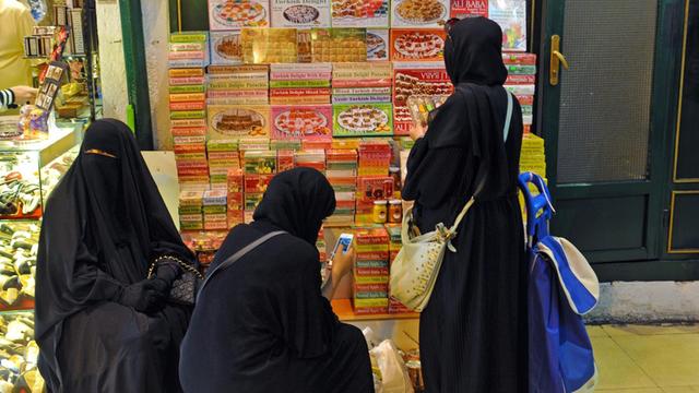 Drei arabische Frauen aus den Golfstaaten in Vollverschleierung und Niqaab machen eine kleine Pause vor einem Stapel türkischer Süssigkeiten, aufgenommen im Großen Basar von Istanbul.