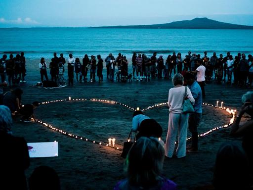 Eine Gruppe Menschen steht am Strand von Auckland in Neuseeland um ein Herz aus Kerzen.
