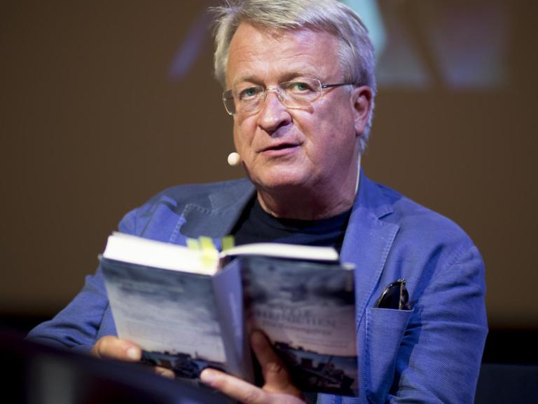 Der Autor Veit Heinichen sitzt auf einer Bühne und liest aus seinem Buch.