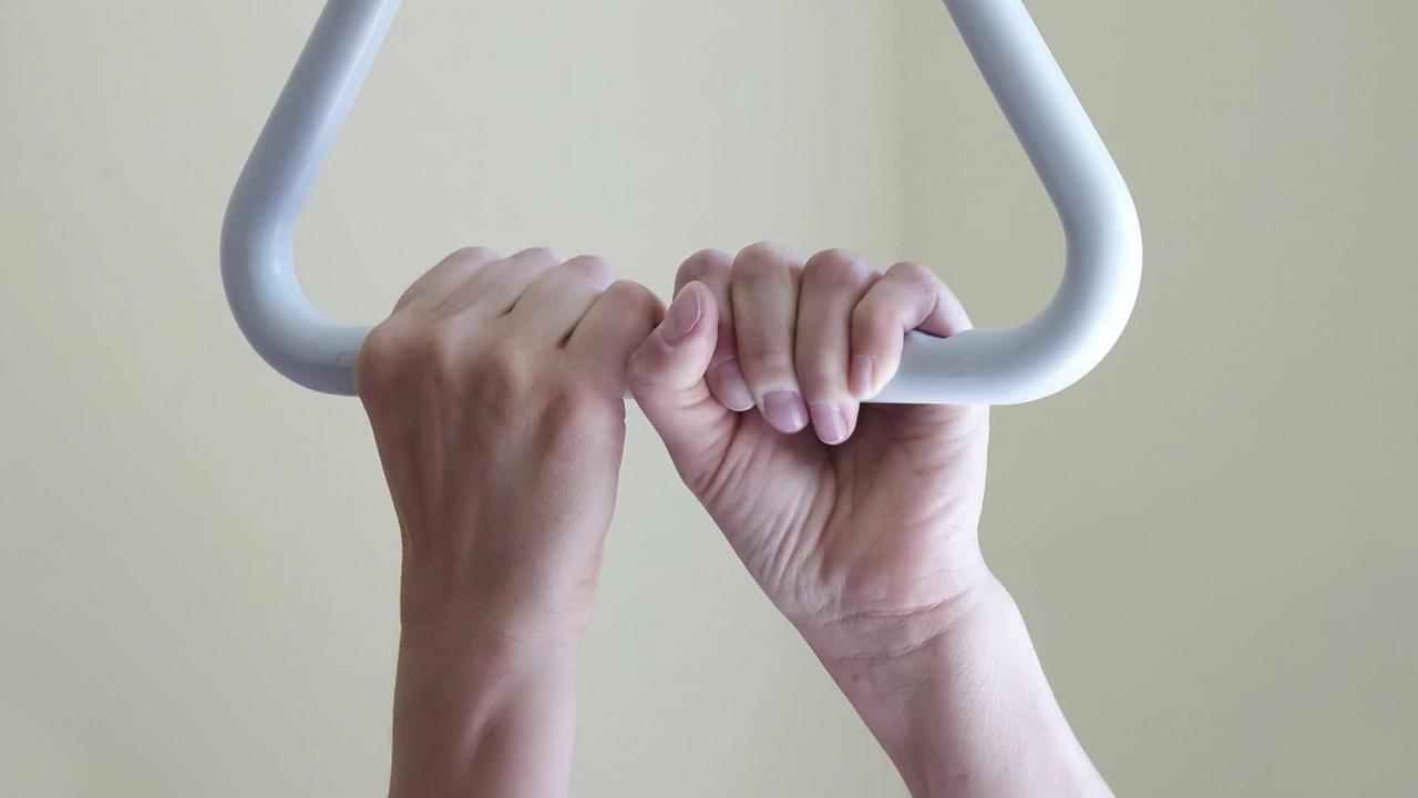 Hände einer älteren Frau, die sich an der Schlaufe eines Krankenhausbetts hochzieht. Hände einer älteren Frau, die sich an der Schlaufe eines Krankenhausbetts hochzieht.