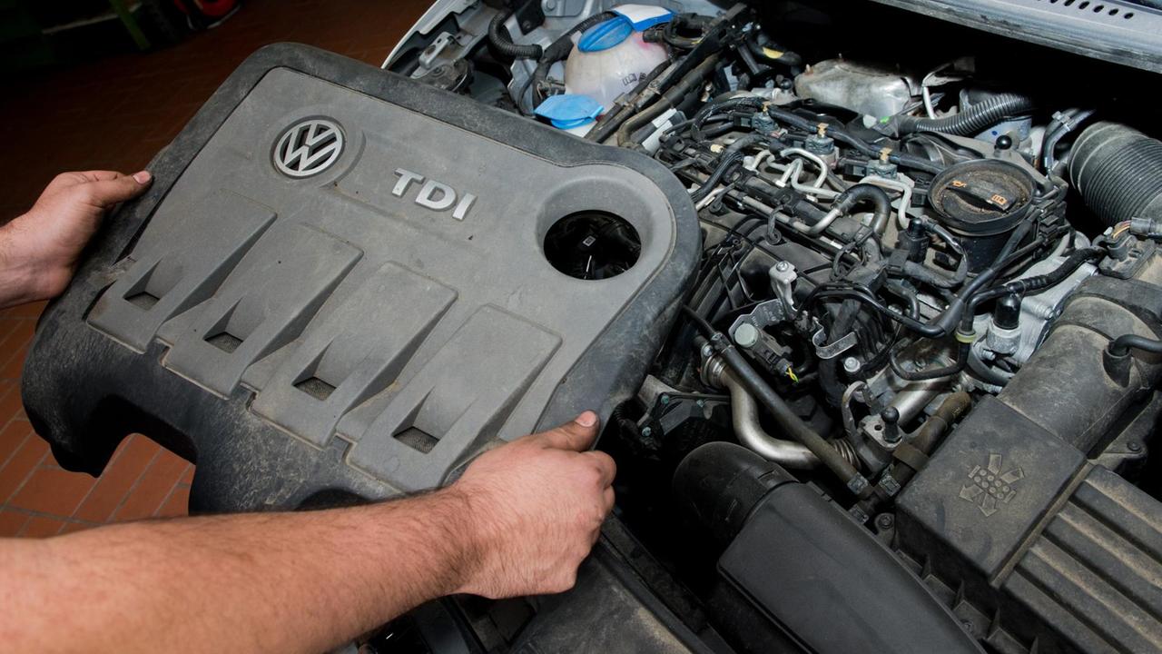 Ein KFZ-Servicetechniker mit einer Abdeckung vor einem vom Abgas-Skandal betroffenen 2.0l TDI Dieselmotor vom Typ EA189 in einem VW Touran in einer Autowerkstatt Ein KFZ-Servicetechniker mit einer Abdeckung vor einem vom Abgas-Skandal betroffenen 2.0l TDI Dieselmotor vom Typ EA189 in einem VW Touran in einer Autowerkstatt
