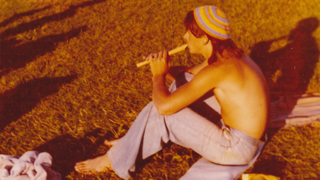 Ein junger Mann mit nacktem Oberkörper sitzt im Sommer 1974 auf dem Deich von Cuxhaven-Döse und spielt Flöte.