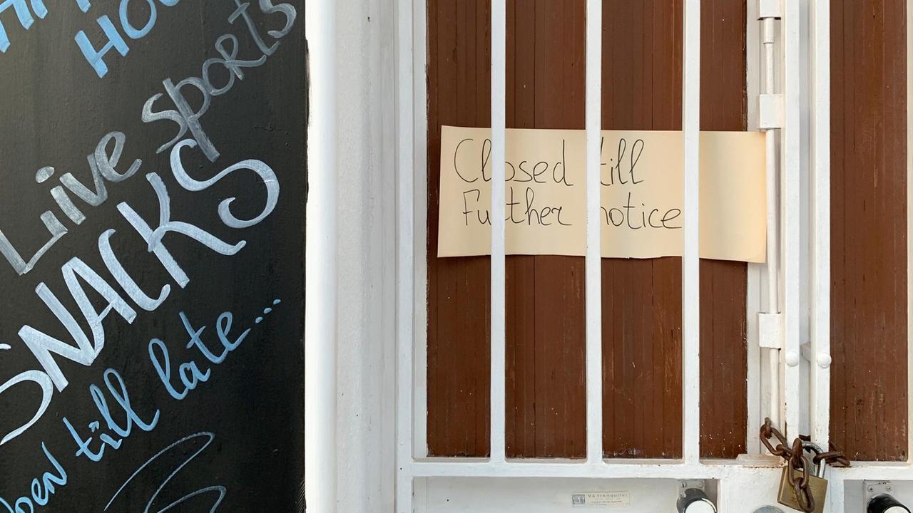 An einer Tür klemmt ein Pappschild, auf dem in englischer Sprache steht: "Bis auf Weiteres geschlossen."