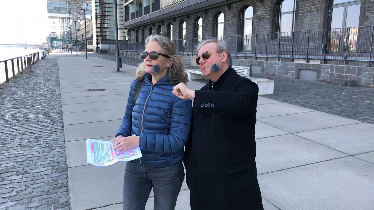 Joachim Król und Deutschlandfunk-Kultur-Reporterin Liane von Billerbeck stehen am Rheinufer in Köln. Im Hintergrund die Kranhäuser am Rheinauhafen. Joachim Król und Deutschlandfunk-Kultur-Reporterin Liane von Billerbeck stehen am Rheinufer in Köln. Im Hintergrund die Kranhäuser am Rheinauhafen.