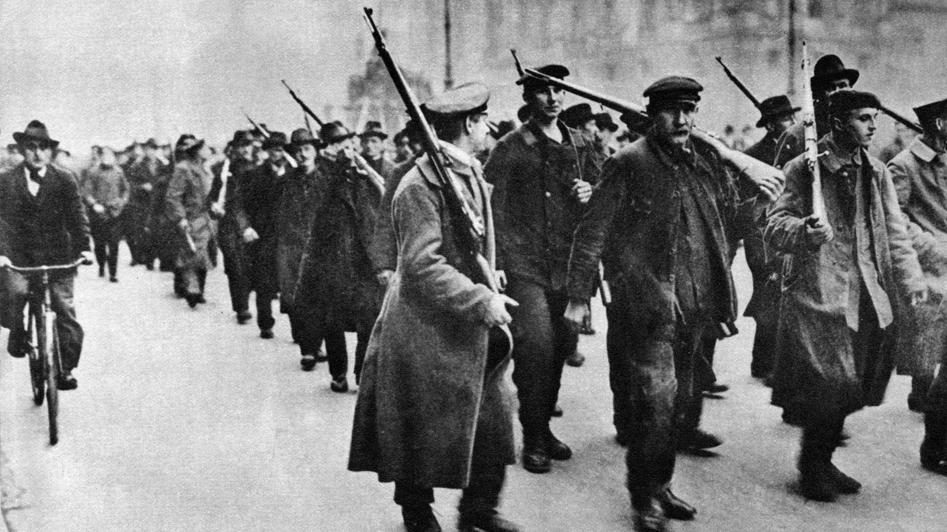 Das Schwarz-Weiß-Foto von 1918 zeigt, wie Aufständische im Zug der Novemberrevolution durch die Straßen Berlins ziehen.