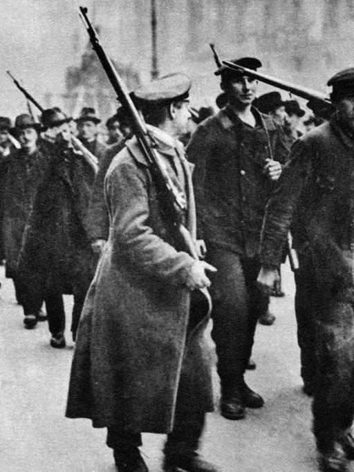 Das Schwarz-Weiß-Foto von 1918 zeigt, wie Aufständische im Zug der Novemberrevolution durch die Straßen Berlins ziehen.