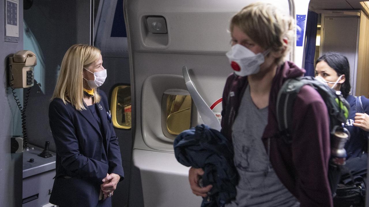 Eine Flugbegleiterin mit Mundschutz begrüßt Passagiere. Eine Flugbegleiterin mit Mundschutz begrüßt Passagiere.