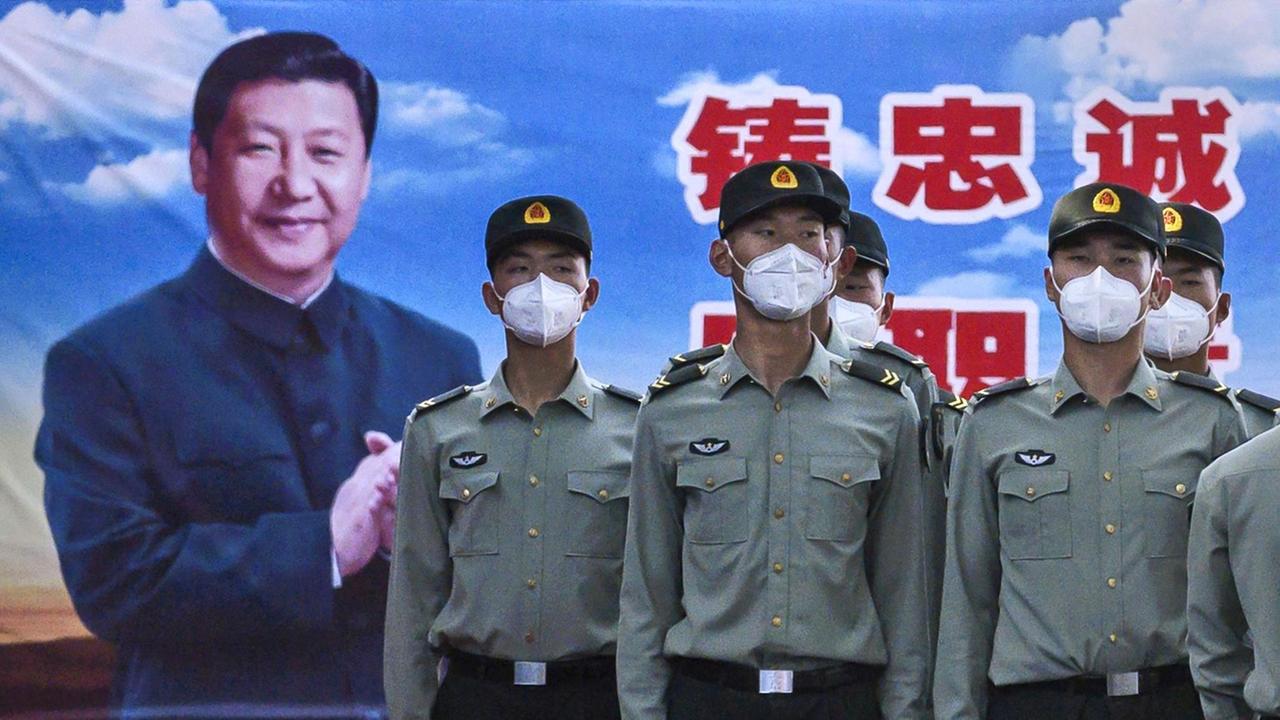 Soldaten mit Mundschutz stehen stramm vor einem Plakat des chinesischen Präsidenten Xi Jinping.