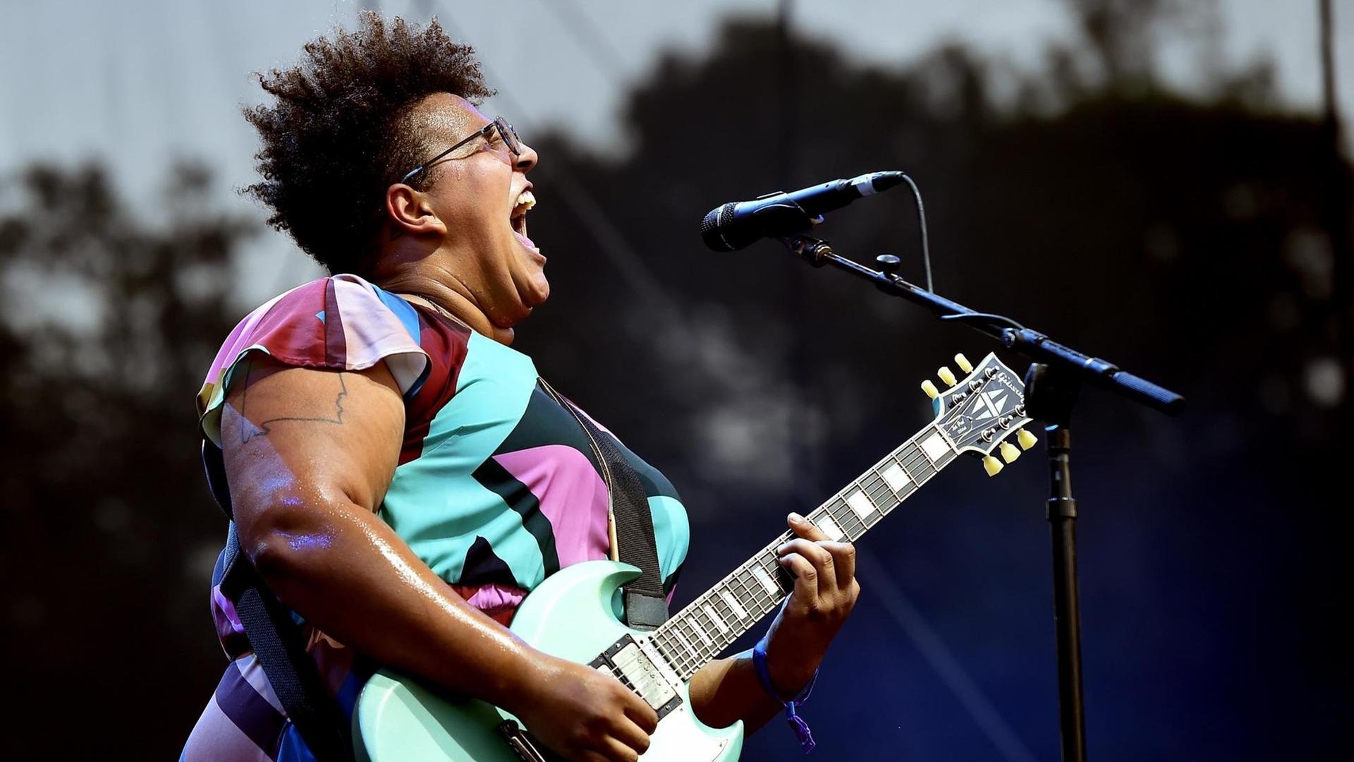 Profilansicht von Brittany Howard mit umgehangener Gitarre singend auf der Bühne. Profilansicht von Brittany Howard mit umgehangener Gitarre singend auf der Bühne.