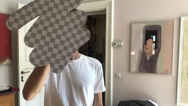 Ein Mann hält ein Schild vor sein Gesicht, dieses sieht aus wie von einem Verpixelungstool erzeugte Manipulation des Bildes.