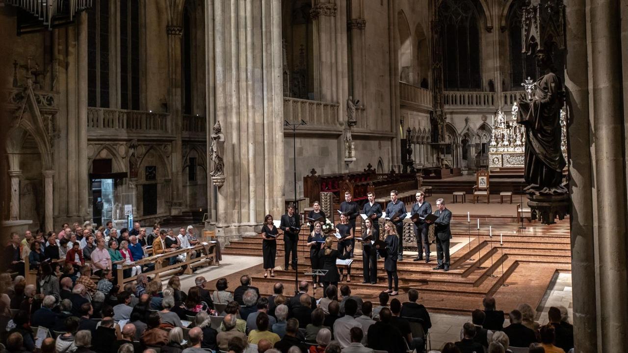 Die ORA Singers werden von Suzi Digby geleitet und gründeten sich 2016 und sind in London beheimatet. Hier sind sie im Halbrund aufgestellt im gotischen Regensburger Dom, die Sängerinnen und Sänger tragen schwarze Konzertkleidung, sie stehen vor dem eigentlichen Altarraum Die ORA Singers werden von Suzi Digby geleitet und gründeten sich 2016 und sind in London beheimatet. Hier sind sie im Halbrund aufgestellt im gotischen Regensburger Dom, die Sängerinnen und Sänger tragen schwarze Konzertkleidung, sie stehen vor dem eigentlichen Altarraum