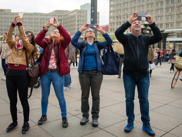 Touristen fotografieren mit ihren Smartphones ein Hochhaus auf dem Alexanderplatz in Berlin.