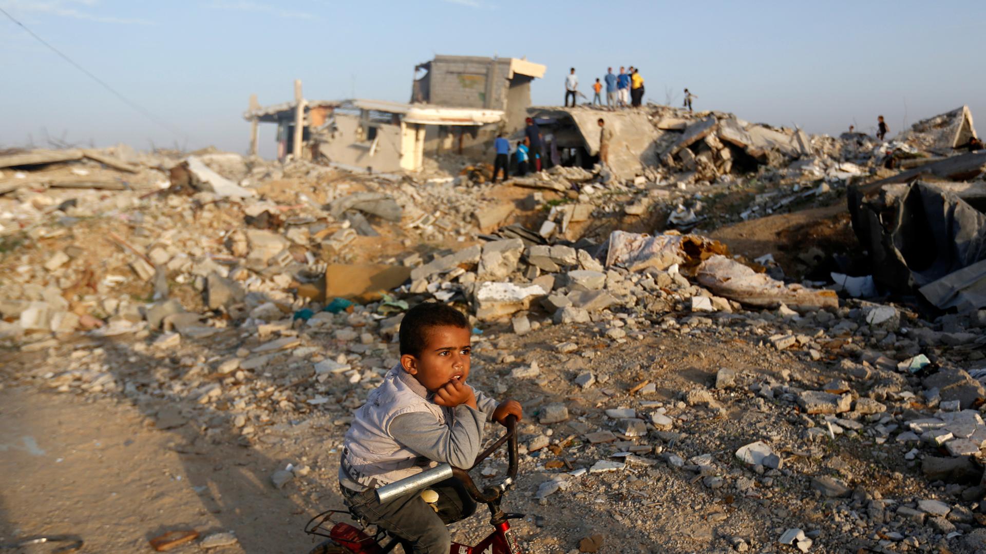 Ein Junge sitzt auf seinem Fahrrad im Gazastreifen inmitten von zerstörten Gebäuden. Ein Junge sitzt auf seinem Fahrrad im Gazastreifen inmitten von zerstörten Gebäuden.