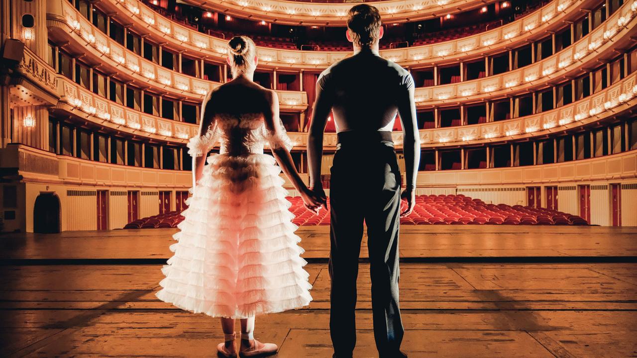 Eine Ballerina und ein Balletttänzer blicken von der Bühne in den Saal der Wiener Staatsoper, der 2.300 Zuschauerplätze hat. Eine Ballerina und ein Balletttänzer blicken von der Bühne in den Saal der Wiener Staatsoper, der 2.300 Zuschauerplätze hat.