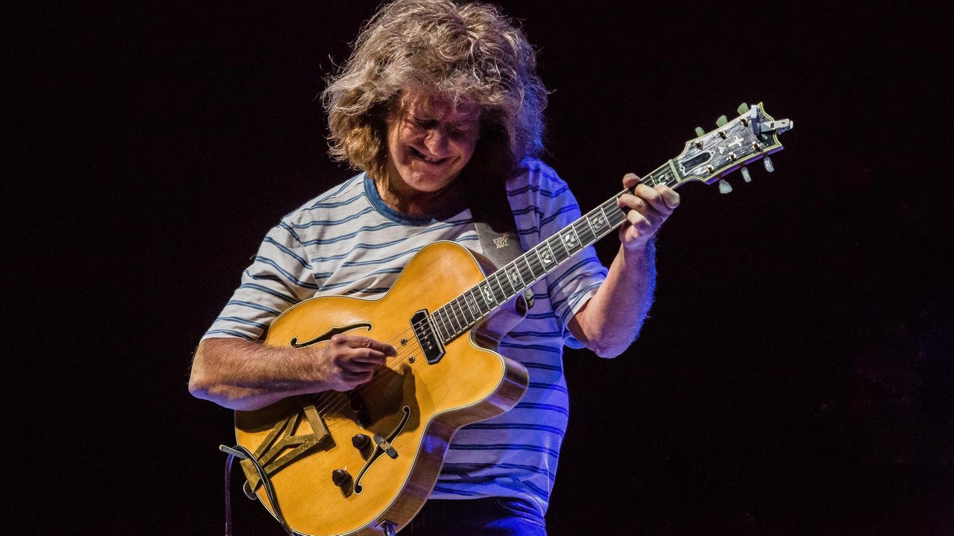 Mit langen Haaren und einem angestrengten Blick spielt Pat Metheney auf der Bühne Gitarre. Mit langen Haaren und einem angestrengten Blick spielt Pat Metheney auf der Bühne Gitarre.