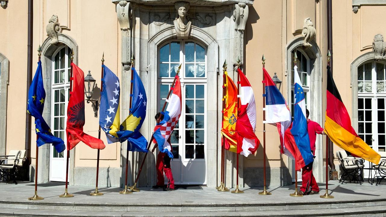 Mitarbeiter des Auswärtigen Amts mühen sich am 28.08.2014 bei der Westbalkan-Konferenz in Berlin vor dem Gruppenbild der Außenminister mit den wehenden Fahnen, die umzukippen drohen. Mitarbeiter des Auswärtigen Amts mühen sich am 28.08.2014 bei der Westbalkan-Konferenz in Berlin vor dem Gruppenbild der Außenminister mit den wehenden Fahnen, die umzukippen drohen.