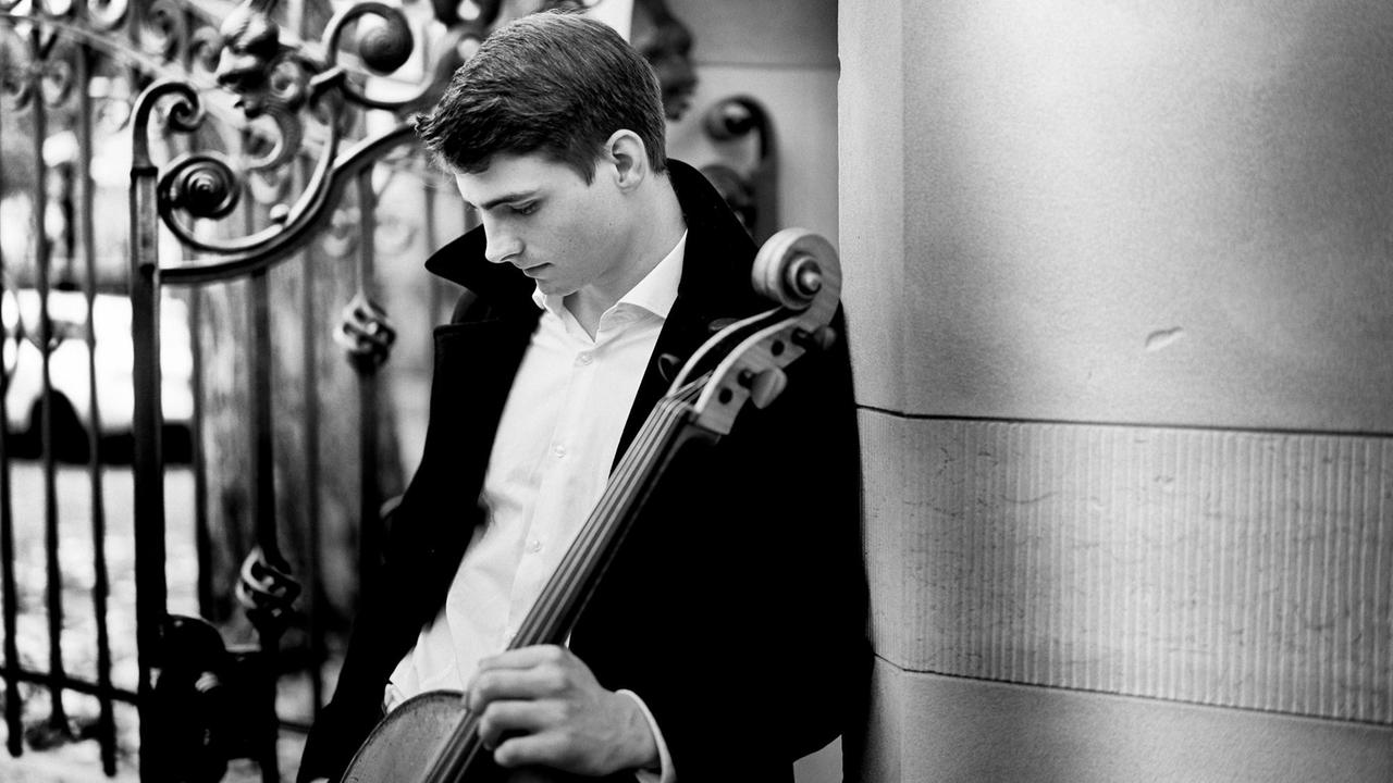 Der Cellist steht an eine Wand gelehnt, vor einem barocken Zaun und hält sein Instrument, auf das er herabblickt. Der Cellist steht an eine Wand gelehnt, vor einem barocken Zaun und hält sein Instrument, auf das er herabblickt.
