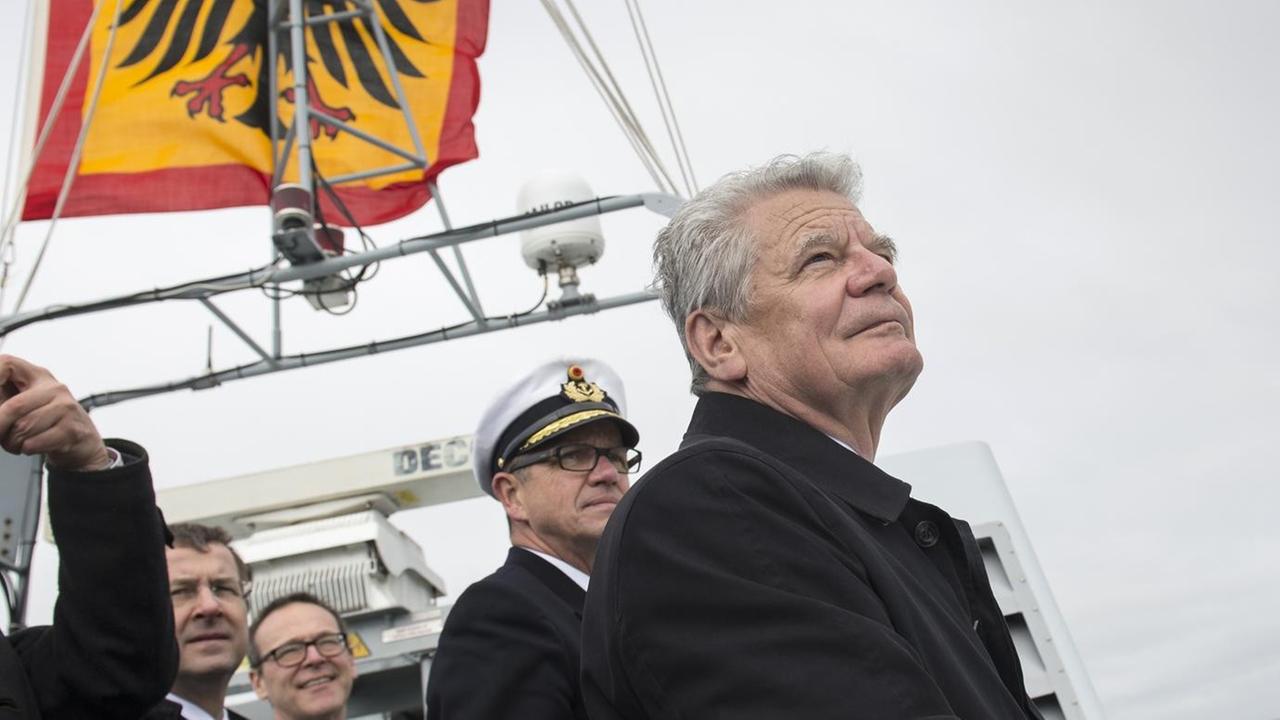 Bundespräsident Joachim Gauck steht auf der deutschen Fregatte "Schleswig-Holstein" und blickt aufs Meer, hinter ihm Offiziere und die deutsche Flagge mit dem Bundesadler. Bundespräsident Joachim Gauck steht auf der deutschen Fregatte "Schleswig-Holstein" und blickt aufs Meer, hinter ihm Offiziere und die deutsche Flagge mit dem Bundesadler.