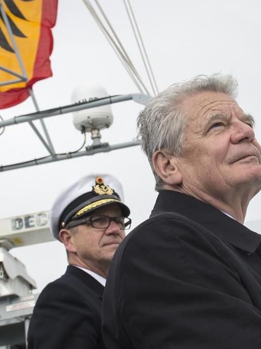 Bundespräsident Joachim Gauck steht auf der deutschen Fregatte "Schleswig-Holstein" und blickt aufs Meer, hinter ihm Offiziere und die deutsche Flagge mit dem Bundesadler.