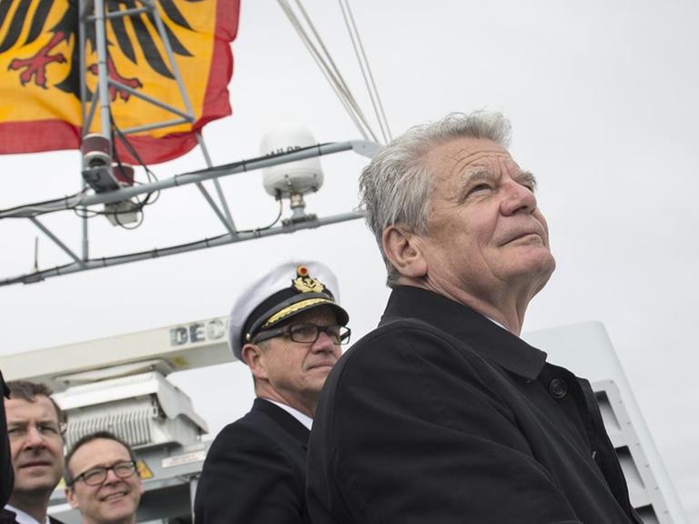 Bundespräsident Joachim Gauck steht auf der deutschen Fregatte "Schleswig-Holstein" und blickt aufs Meer, hinter ihm Offiziere und die deutsche Flagge mit dem Bundesadler.