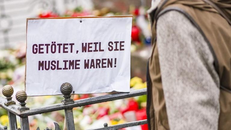 Eine Frau steht auf dem Marktplatz in Hanau vor dem Denkmal der Brüder Grimm. Vor dem Denkmal stehen Blumen, Kerzen und ein Plakat mit der Aufschrift «Getötet, weil sie Muslime waren». Eine Frau steht auf dem Marktplatz in Hanau vor dem Denkmal der Brüder Grimm. Vor dem Denkmal stehen Blumen, Kerzen und ein Plakat mit der Aufschrift «Getötet, weil sie Muslime waren».
