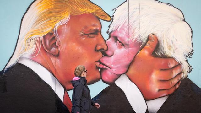 Frau geht an einem Wandbild vorbei, das auf ein verfallenes Gebäude in Stokes Croft gemalt wurde und den hoffnungsvollen US-Präsidenten Donald Trump zeigt, der am 24. Mai 2016 in Bristol, England, einen Kuss mit dem ehemaligen Londoner Bürgermeister Boris Johnson teilt