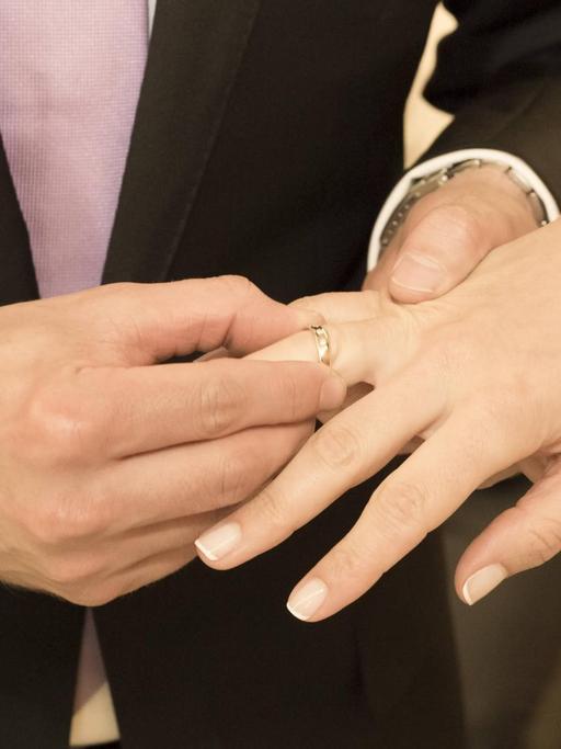 Ein Brautpaar streift sich gegenseitig den Ring über die Finger.