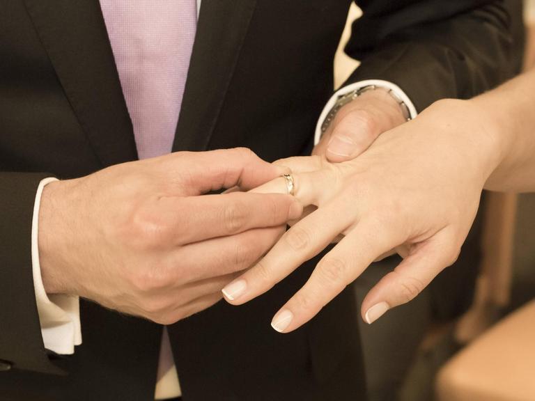 Ein Brautpaar streift sich gegenseitig den Ring über die Finger.
