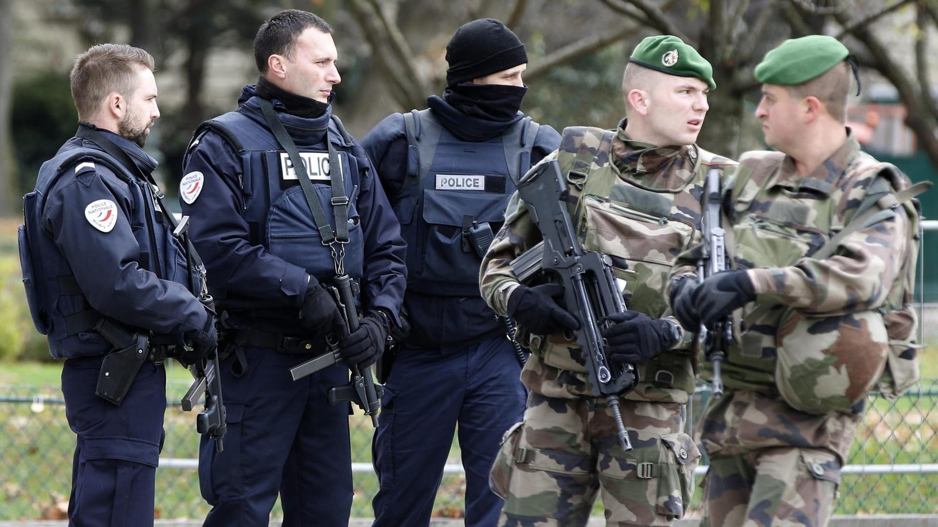 Drei Polizisten in blauer und zwei Soldaten in olivgrüner Uniform stehen zusammen. Drei Polizisten in blauer und zwei Soldaten in olivgrüner Uniform stehen zusammen.