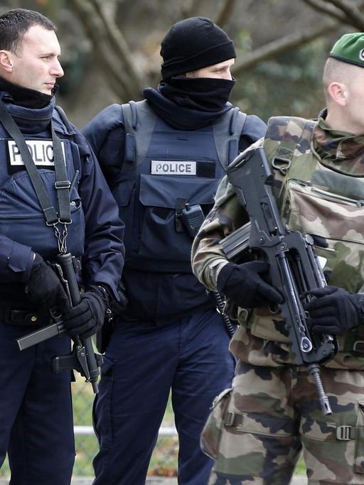 Drei Polizisten in blauer und zwei Soldaten in olivgrüner Uniform stehen zusammen.