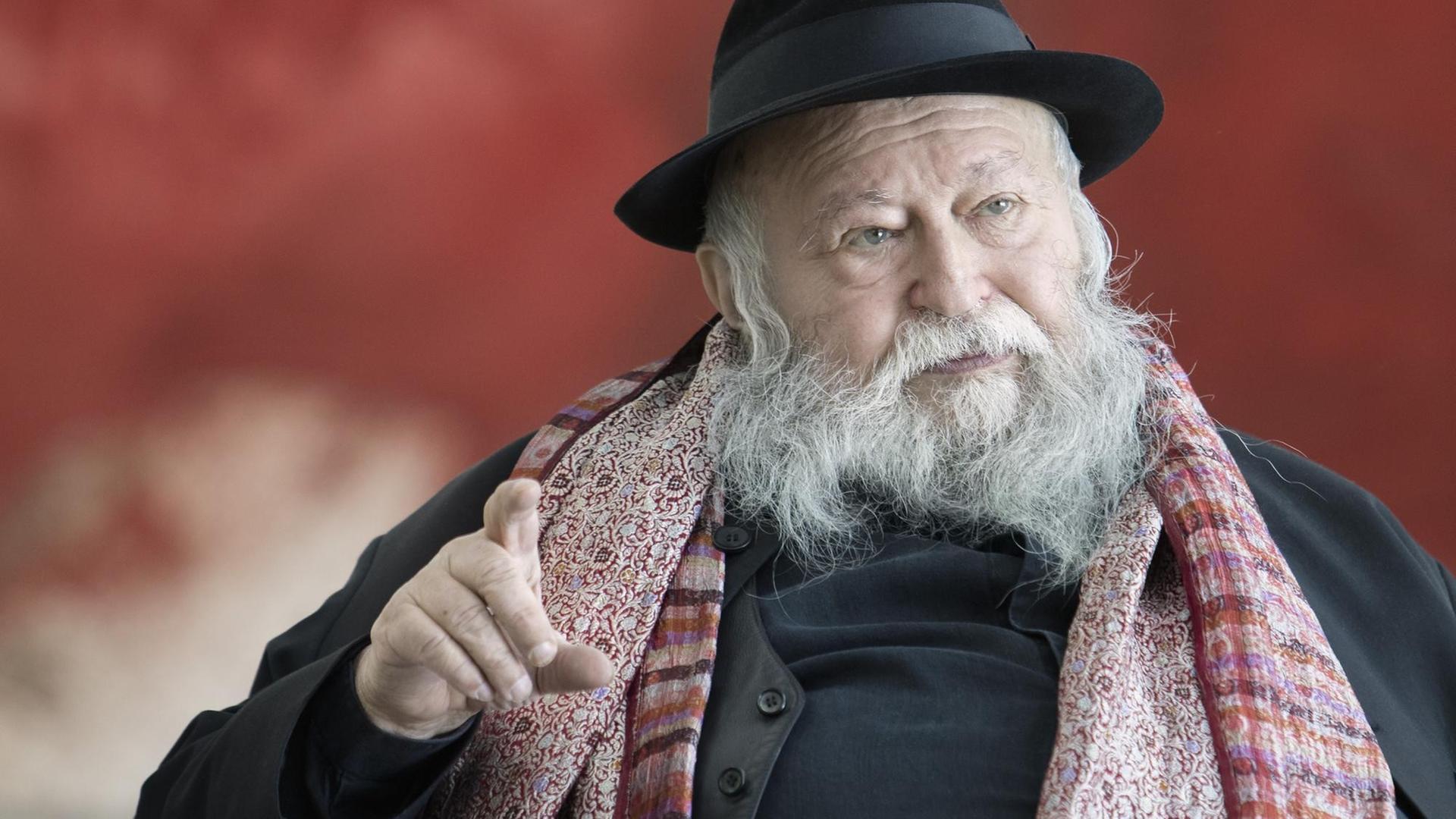 Hermann Nitsch, mit Vollbart und Hut, sitzt vor einer roten Wand und unterhält sich mit dem Fotografen. Hermann Nitsch, mit Vollbart und Hut, sitzt vor einer roten Wand und unterhält sich mit dem Fotografen.