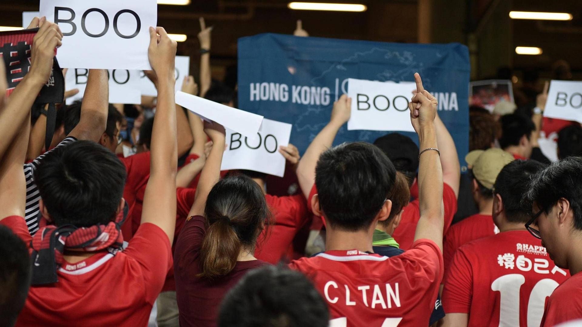 Fußballfans drehen dem Spiel zwischen Iran und Hongkong den Rücken zu und halten Schilder hoch, auf denen "Boo" steht.