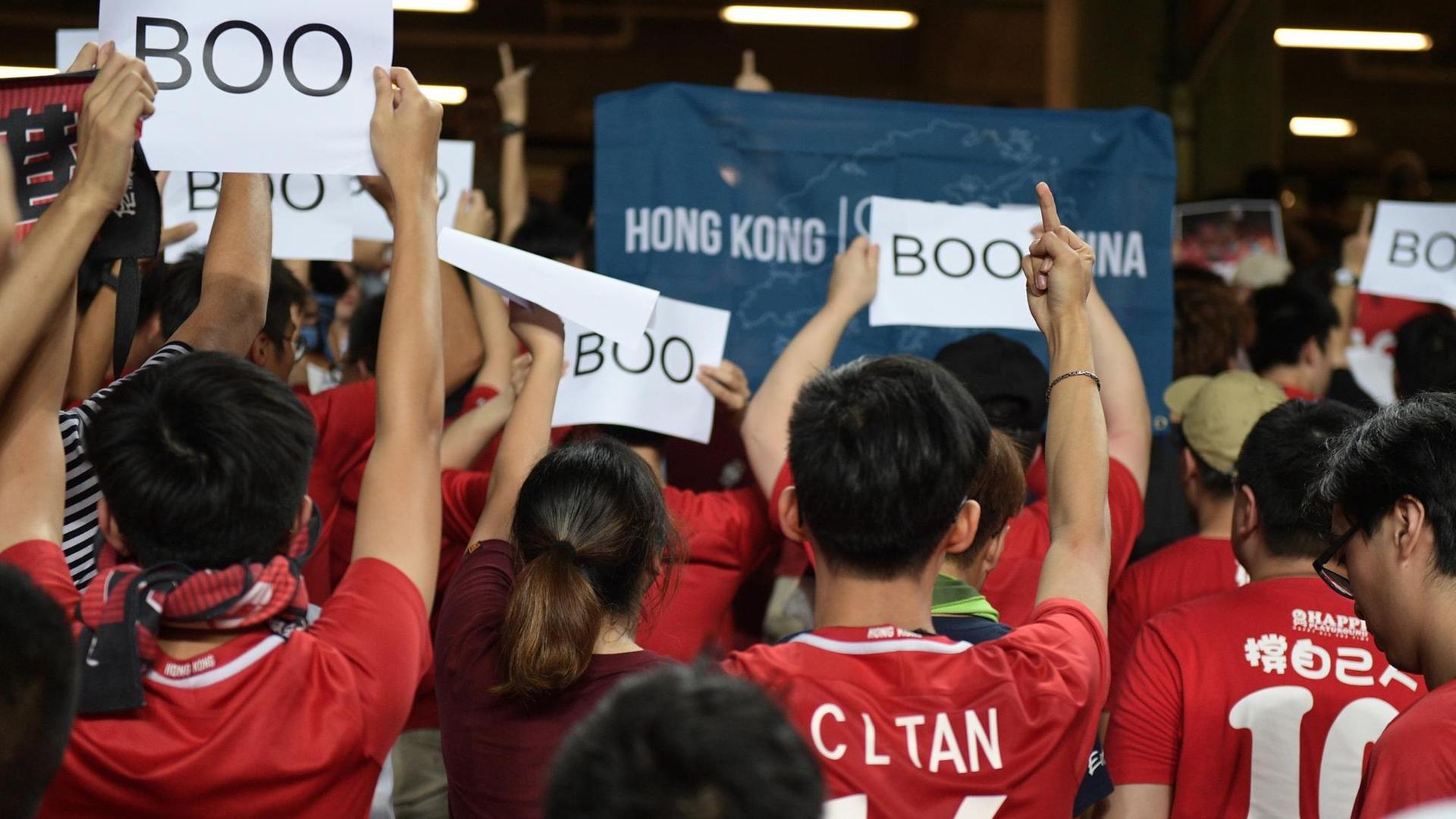 Fußballfans drehen dem Spiel zwischen Iran und Hongkong den Rücken zu und halten Schilder hoch, auf denen "Boo" steht. Fußballfans drehen dem Spiel zwischen Iran und Hongkong den Rücken zu und halten Schilder hoch, auf denen "Boo" steht.