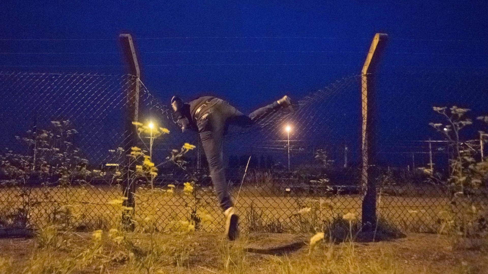 Ein Flüchtling klettert auf das Gelände des Eurotunnels in Calais. Ein Flüchtling klettert auf das Gelände des Eurotunnels in Calais.