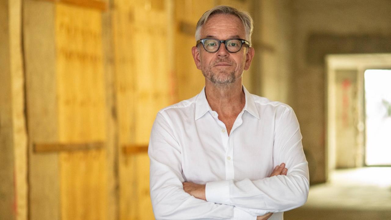 Porträt von Oliver Reese. Der Intendant des Berliner Ensemble steht vor der Baustelle des neuen Gebäudes. Er trägt ein weißes Hemd und hat die Arme vor der Brust verschränkt. Porträt von Oliver Reese. Der Intendant des Berliner Ensemble steht vor der Baustelle des neuen Gebäudes. Er trägt ein weißes Hemd und hat die Arme vor der Brust verschränkt.