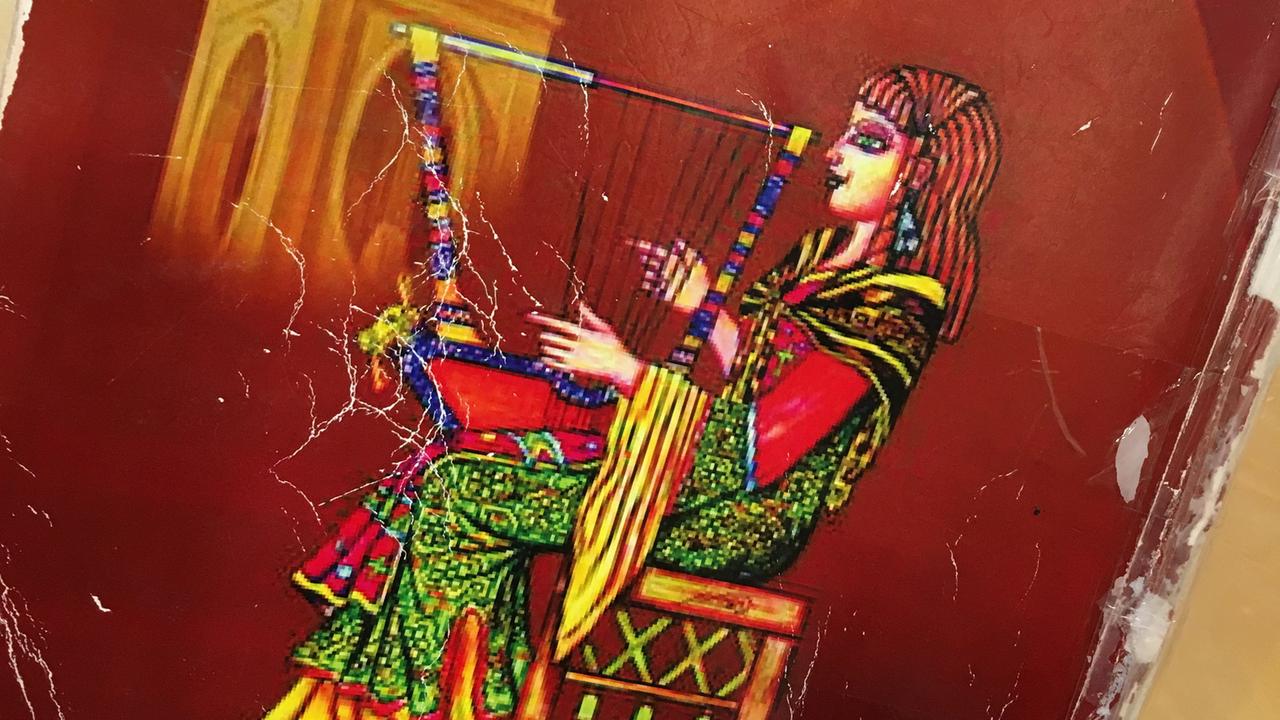 Der abgegriffene Einband des Gesangbuches des syrisch-katholischen Chors "Sonne der Aramäer" in Köln. Das Bild zeigt eine Frau in traditionellem Gewand, die Harfe spielt. Der abgegriffene Einband des Gesangbuches des syrisch-katholischen Chors "Sonne der Aramäer" in Köln. Das Bild zeigt eine Frau in traditionellem Gewand, die Harfe spielt.