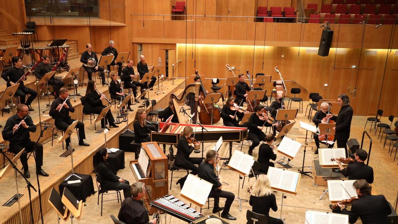 Orchestermusiker mit Cembalo sitzten in größere Abständen voneinander und spielen nach Weisungen des Dirigenten. Orchestermusiker mit Cembalo sitzten in größere Abständen voneinander und spielen nach Weisungen des Dirigenten.